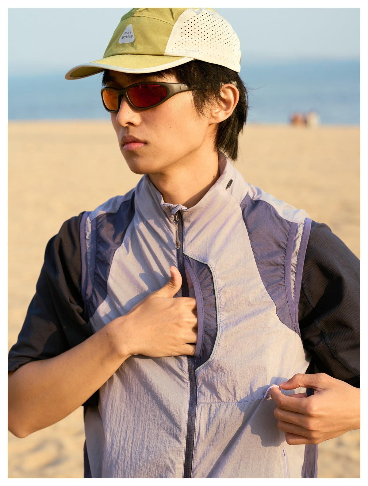 Close view of a model opening the front pocket of a light gray-lavender zip vest with dark contrast panels.
