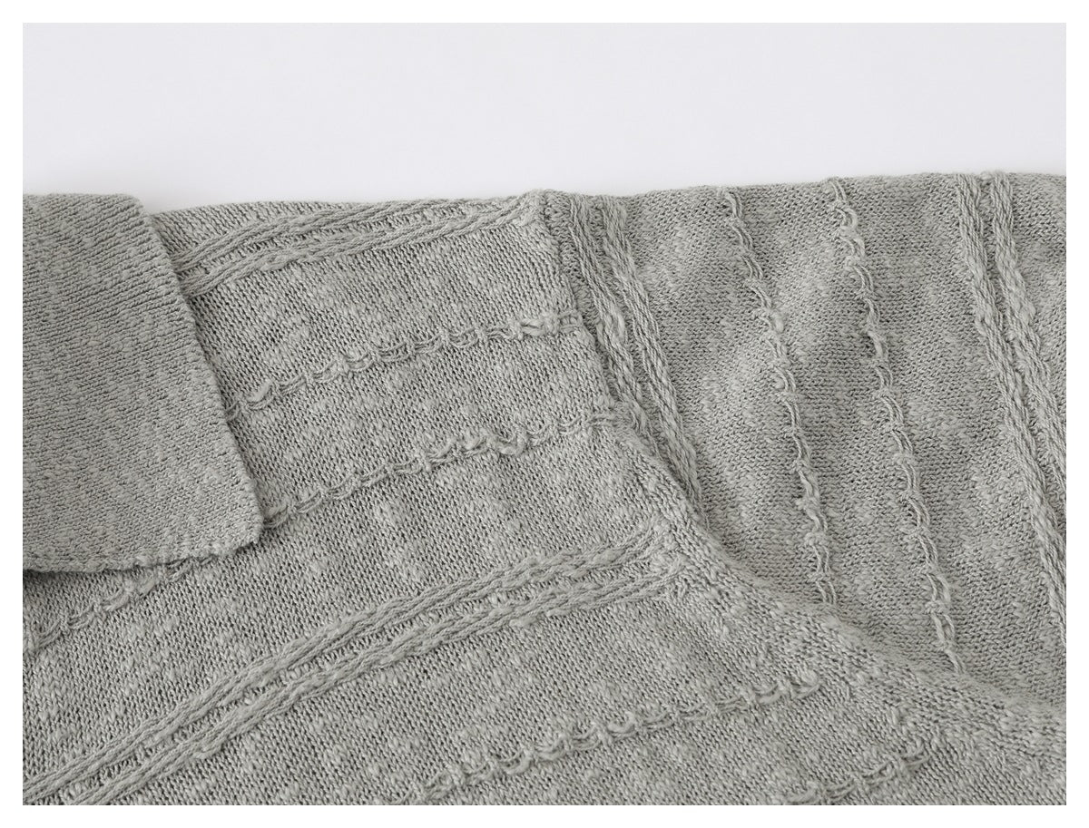 Close-up of a light gray knitted garment with raised cable and looped stitch patterns.