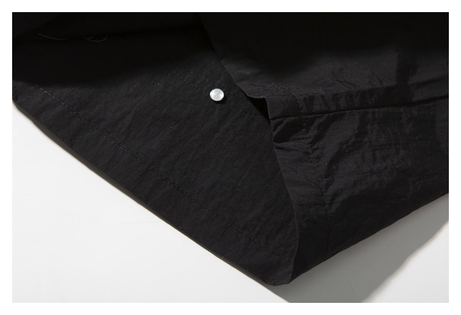 Close-up of black garment fabric with a stitched seam and a small silver snap.
