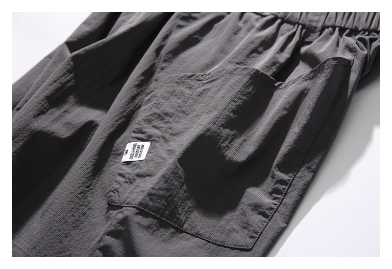 Close-up of dark gray pants with an elastic waistband, large patch pockets, and a small white sewn-in label.