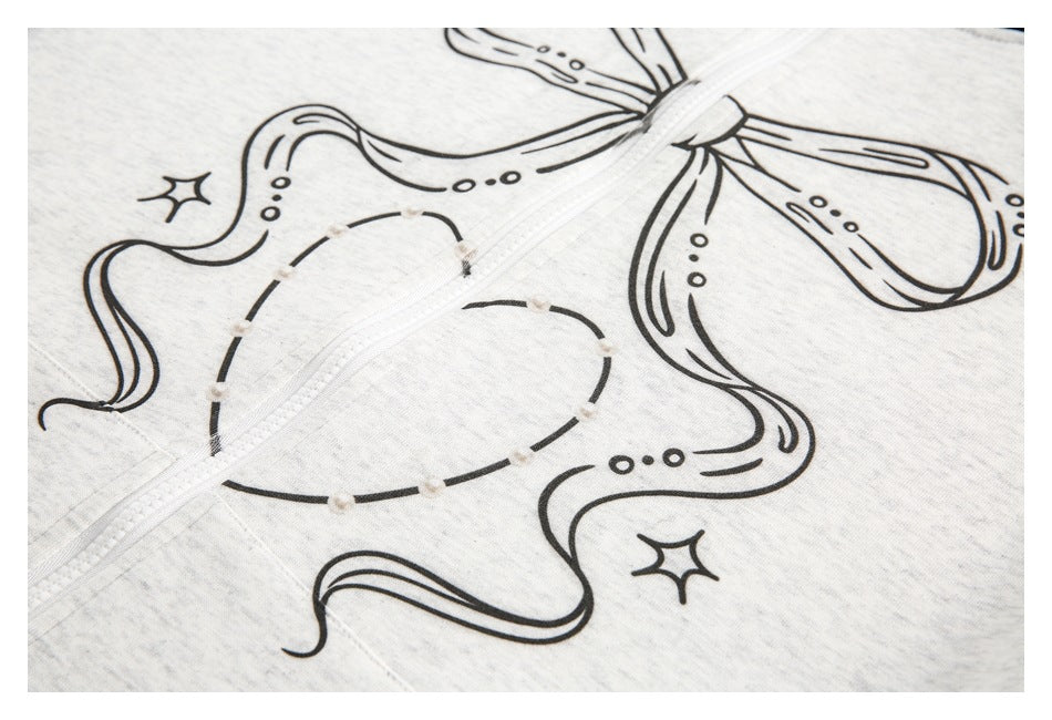 Close-up of a light gray heather zip-up garment with a black bow-and-star graphic and white zipper.
