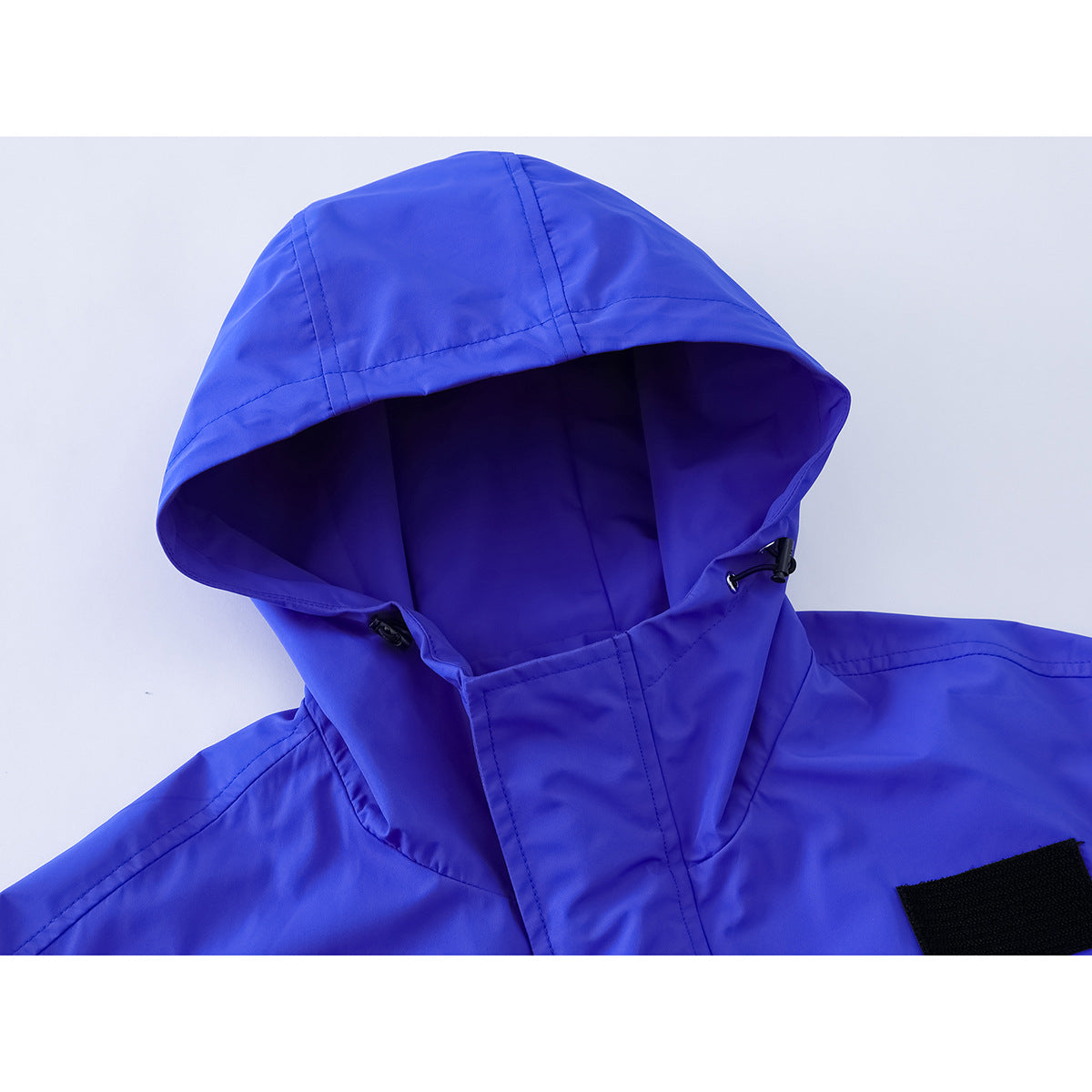 Close-up of a bright blue jacket hood with adjustable toggles and a black hook-and-loop patch.