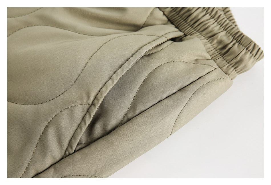 Close-up of an olive quilted pants pocket opening and curved stitching.