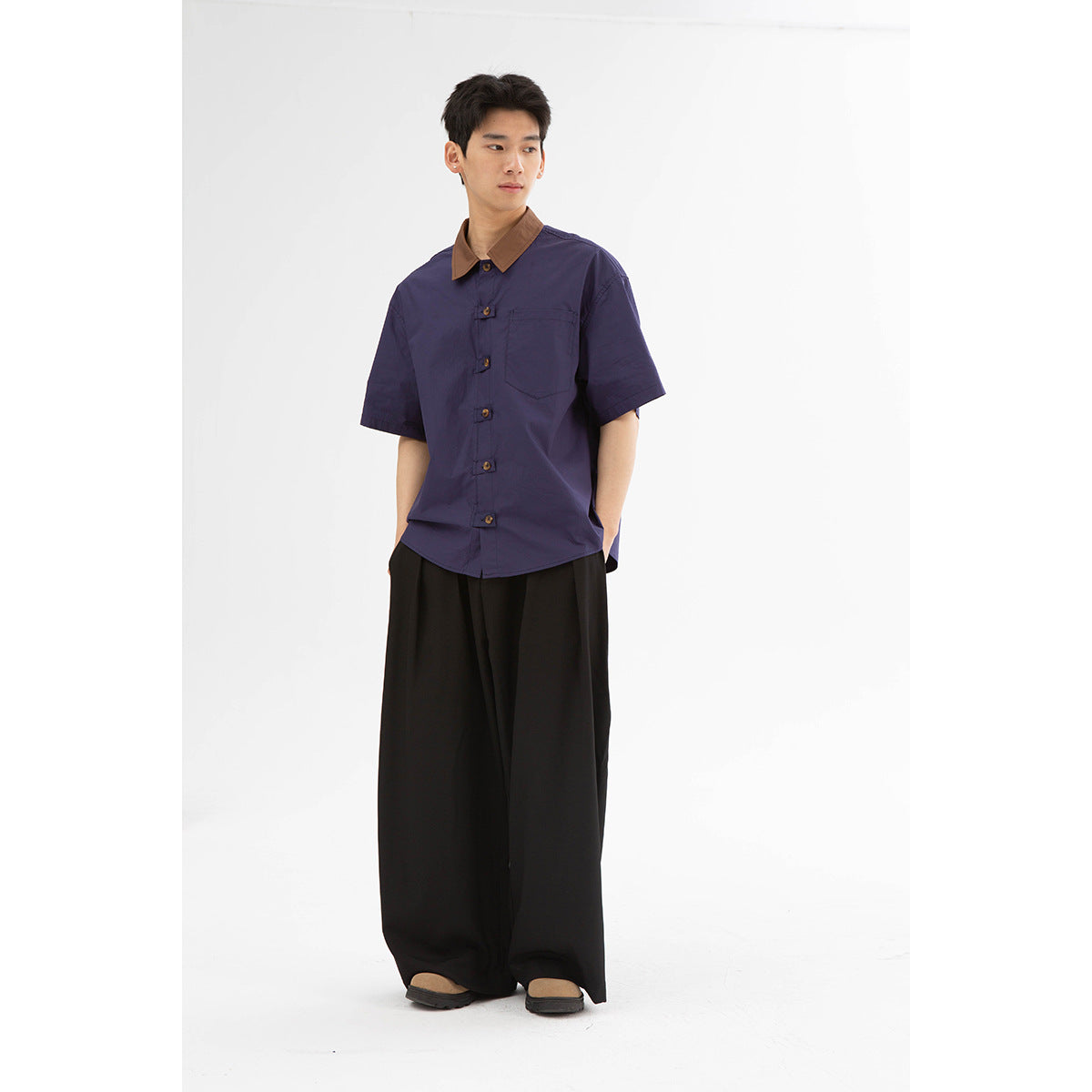 Model wearing a dark purple short-sleeve button-up shirt with a brown collar and black wide-leg trousers.