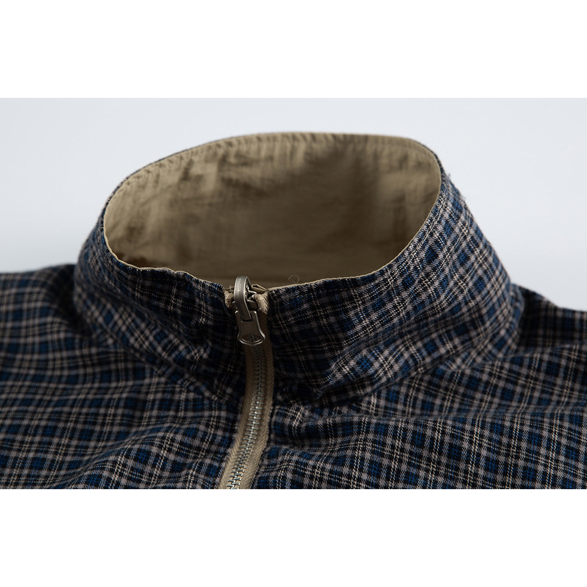 Close-up of a navy, gray and tan plaid jacket's stand collar and beige lining around the front zipper.