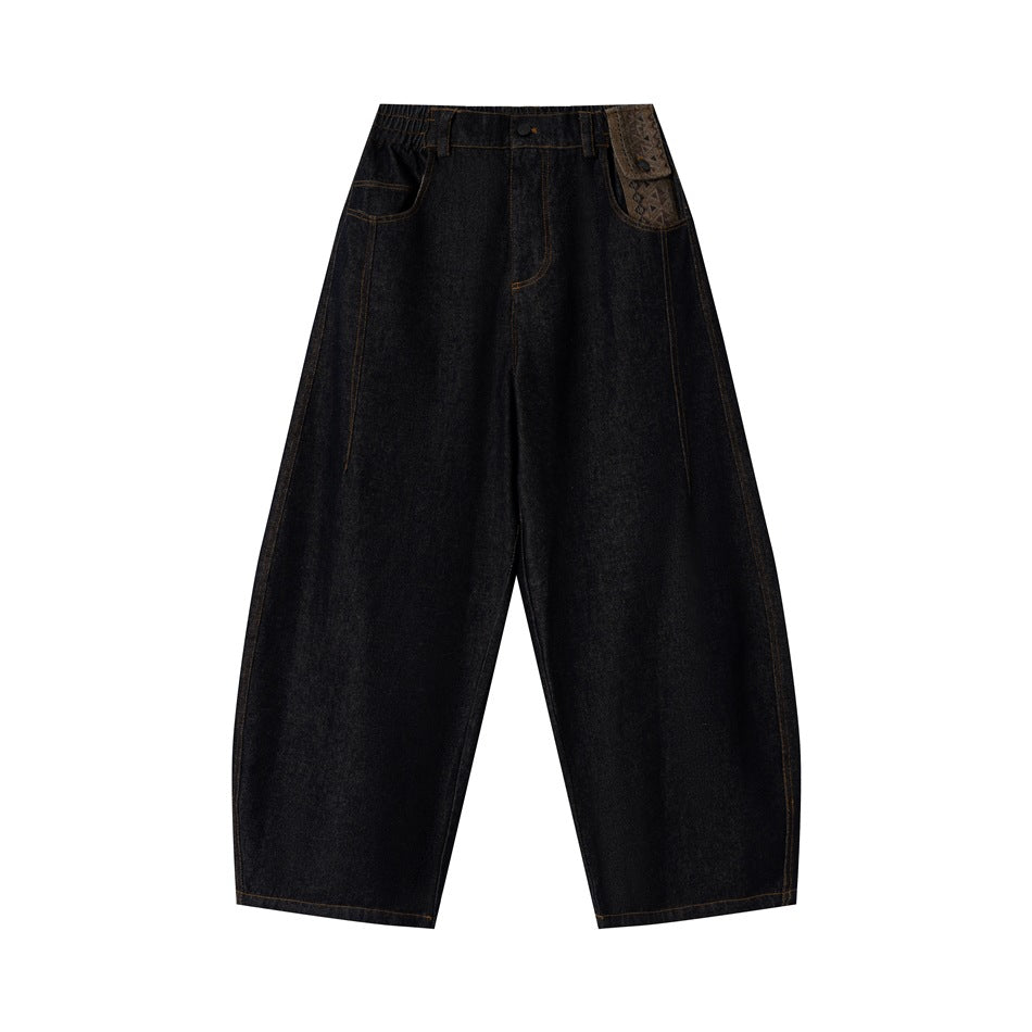 Dark blue barrel-leg denim jeans flat front view with patterned right pocket panel and orange topstitching