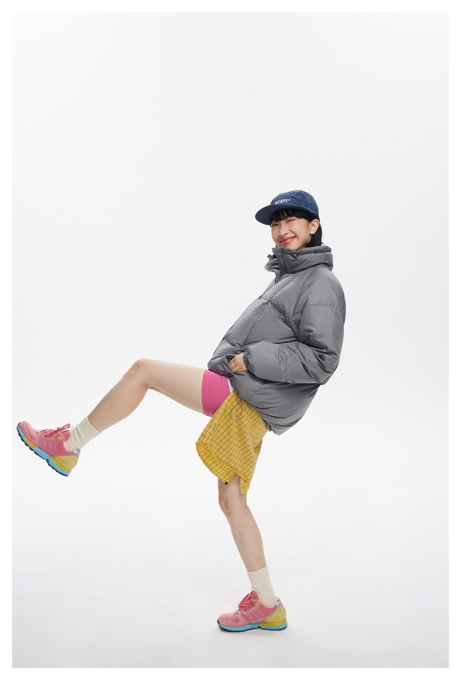 Model wearing a charcoal-gray puffer jacket, shown in a playful full-body pose.