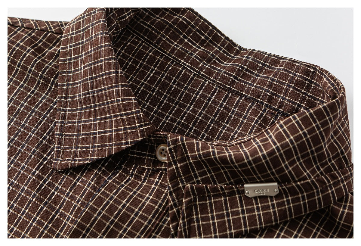 Close-up of a brown plaid shirt collar with a button and small metal badge.
