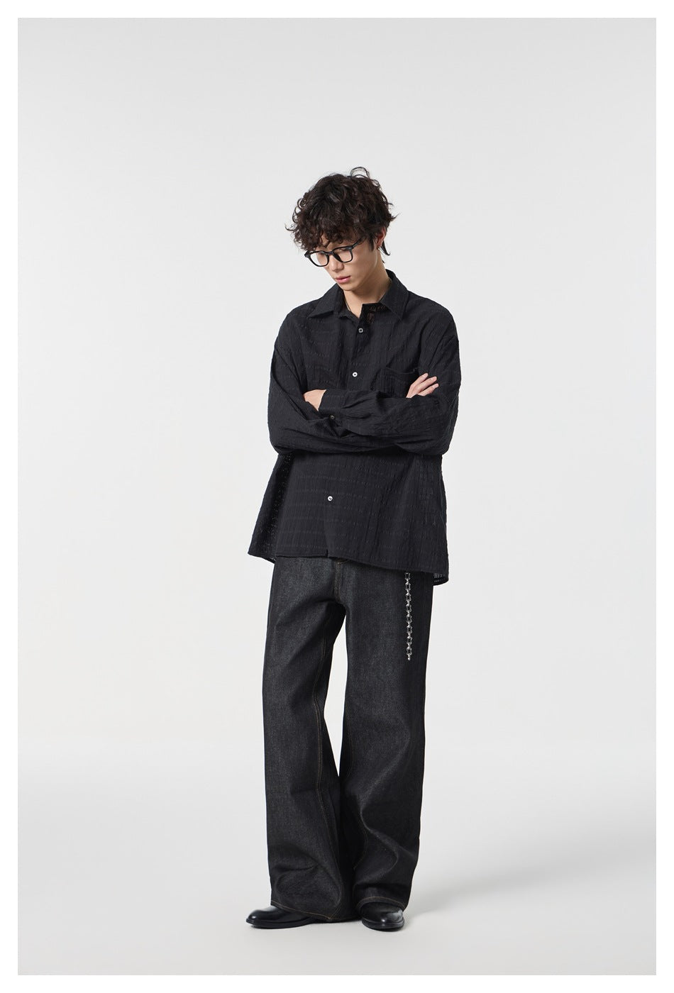 Model wearing a black long-sleeve button-up shirt with a chest pocket and dark wide-leg jeans.