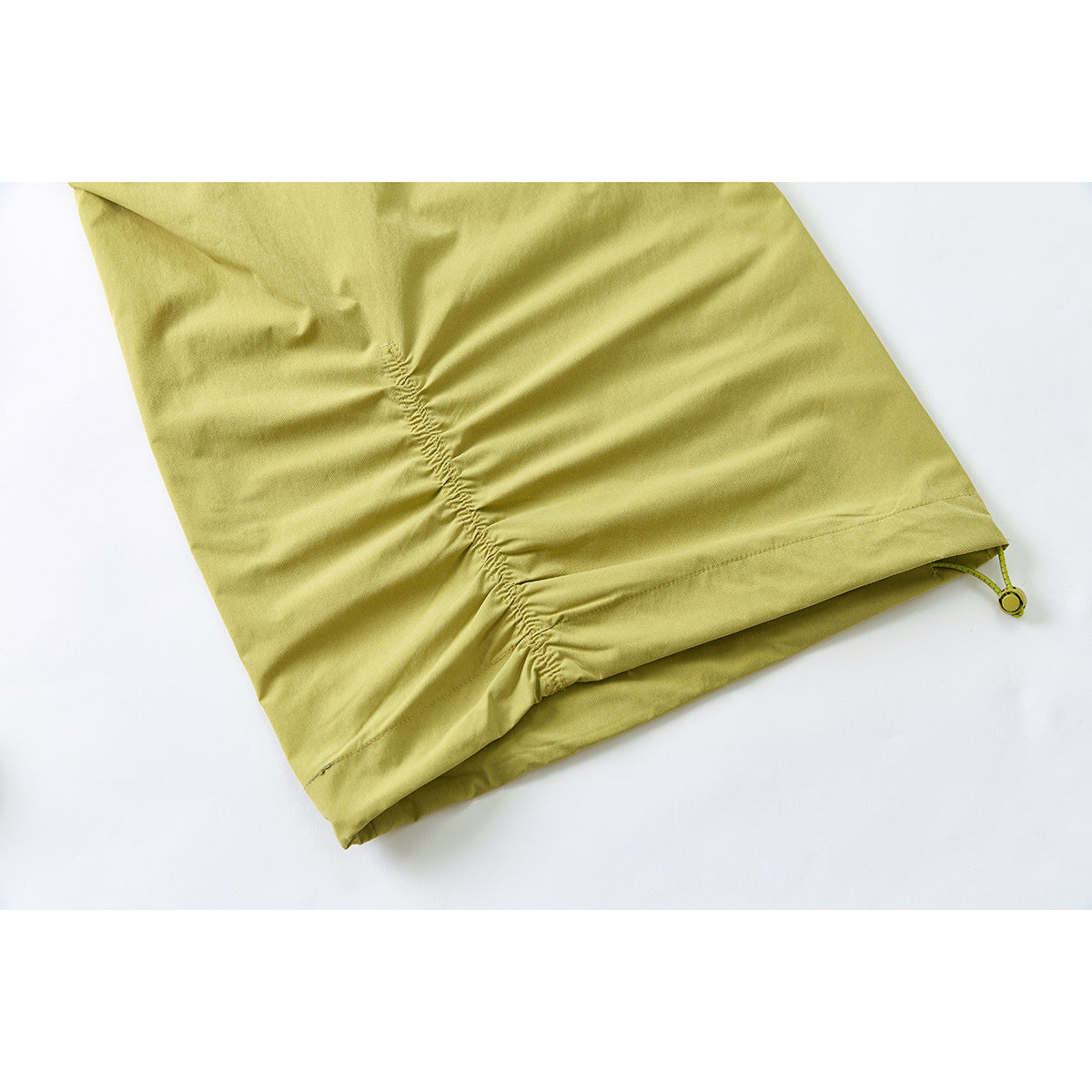 Close-up of a mustard yellow-green trouser leg hem with gathered ruching and an adjustable cord toggle.