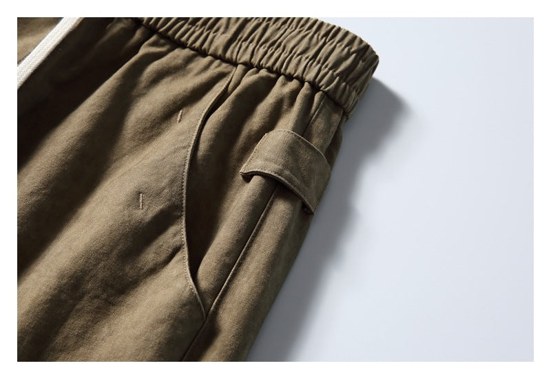 Close-up of olive-brown pants showing a curved side pocket and a small fabric tab.