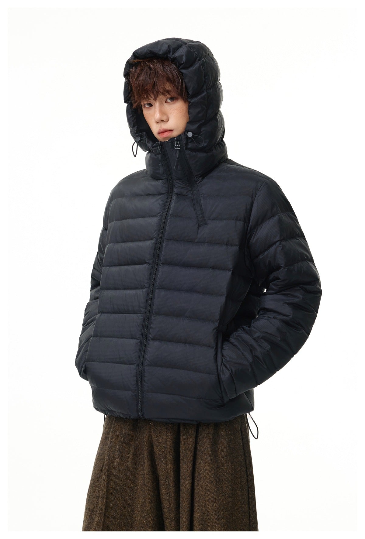 Model wearing a black quilted jacket zipped to the neck, with its adjustable hood raised.