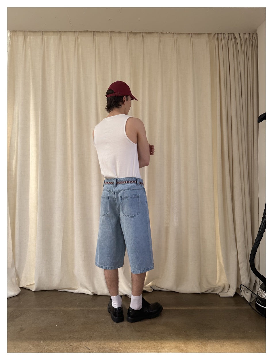 Rear view of a model wearing light blue denim knee-length shorts with a patterned waistband and a white tank top.