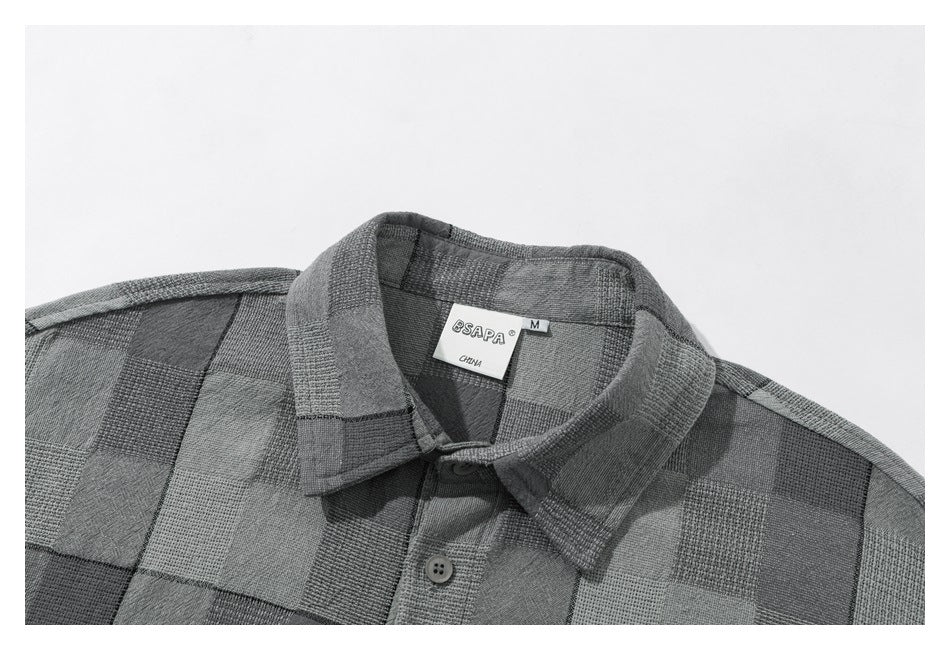 Close-up of a gray patchwork-check shirt showing its pointed collar, button placket, and sewn-in neck label.