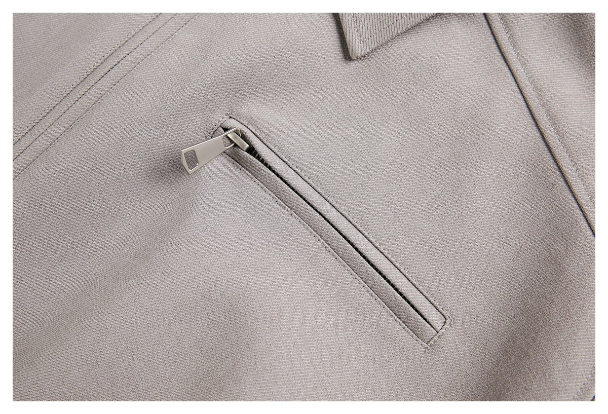 Close-up of a taupe jacket with a slanted zippered pocket and metal pull.