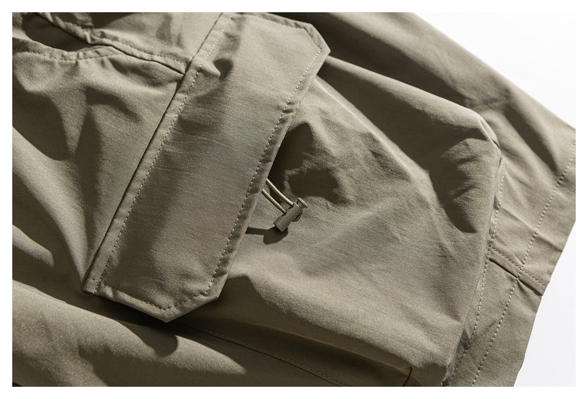 Close-up of an olive garment's stitched flap pocket and small drawcord toggle.
