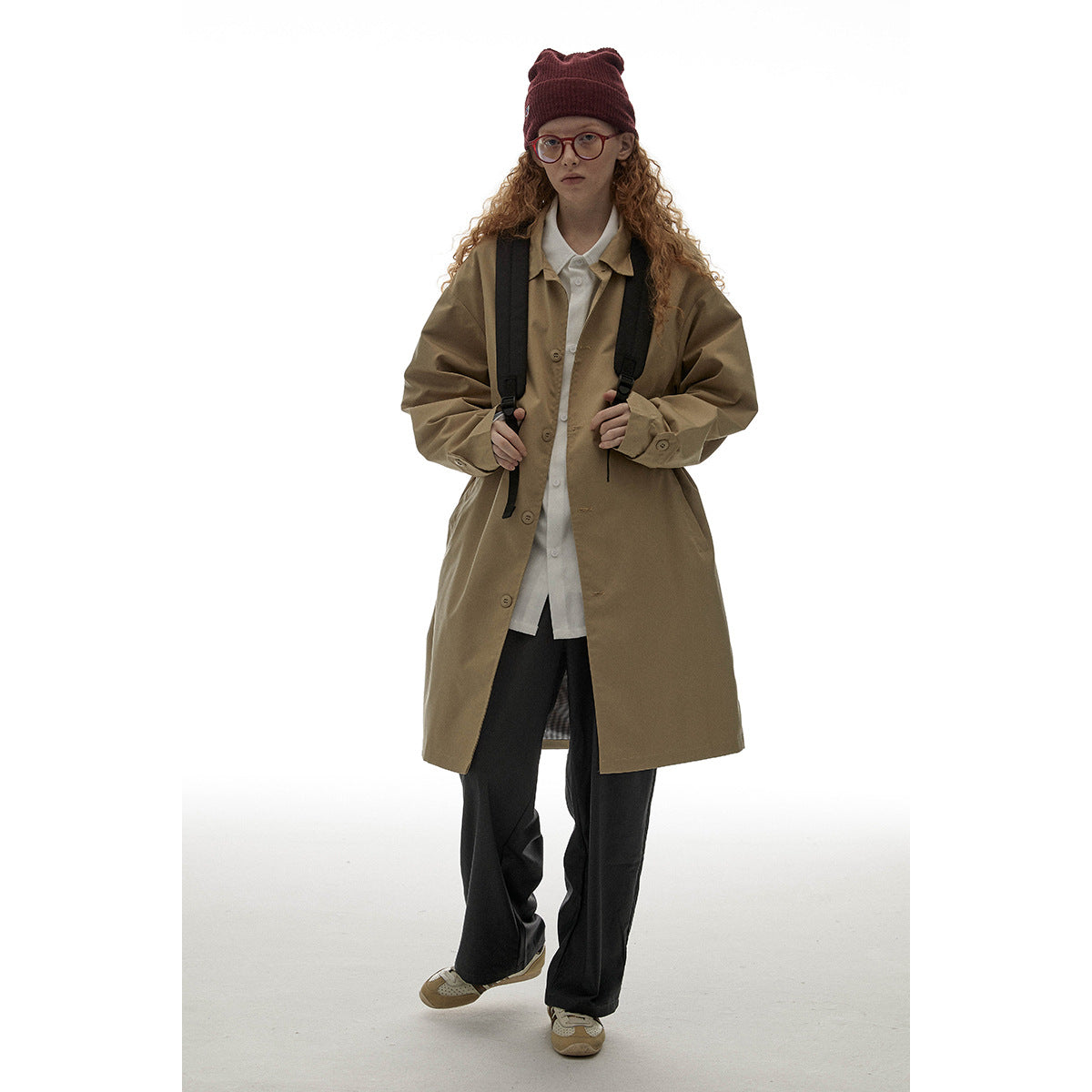 Model wearing a long tan button-front coat over a white shirt and black trousers.
