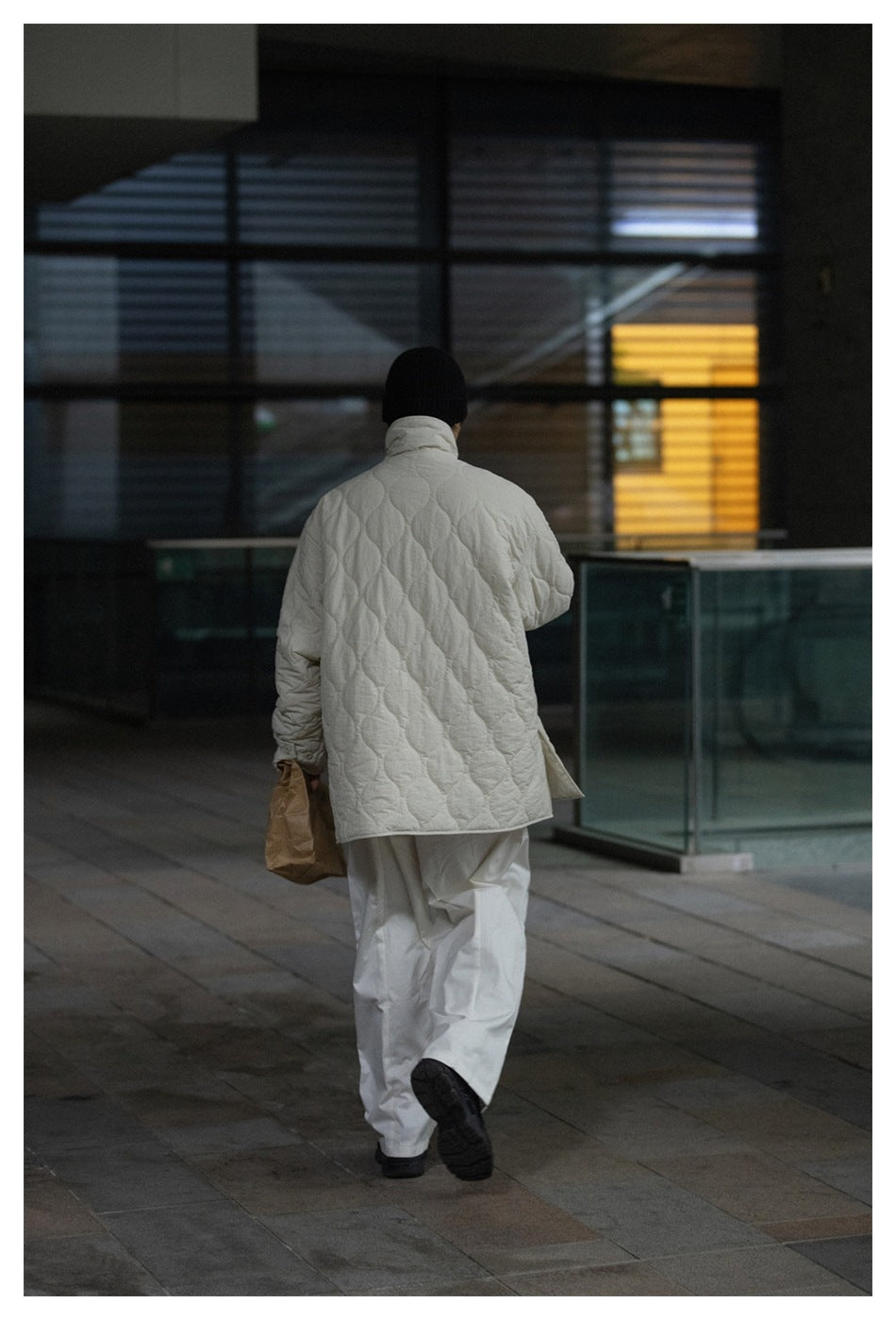 Back view of a person walking in an off-white quilted jacket, white trousers and black beanie