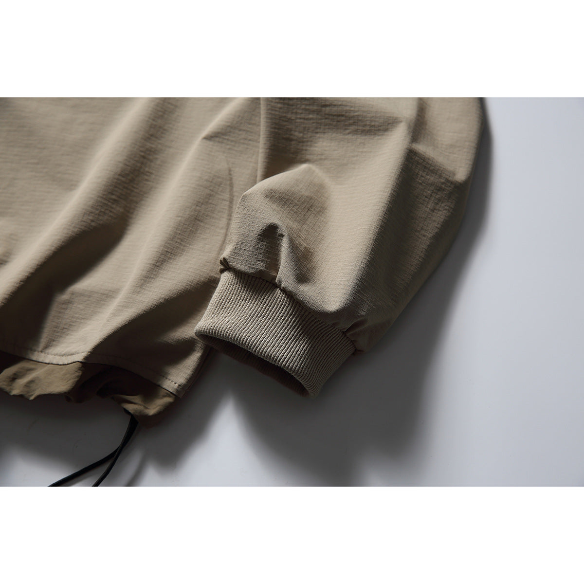 Close-up of a taupe pullover sleeve showing its ribbed cuff and adjustable drawcord hem.