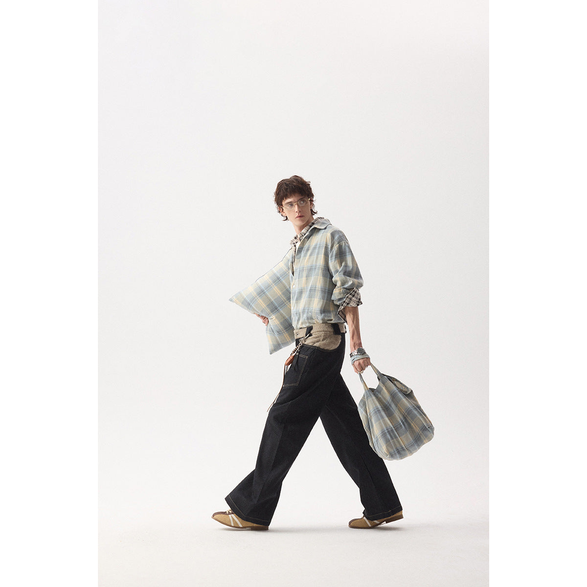 Model walking in a blue-gray plaid shirt with rolled sleeves, carrying a matching plaid tote.