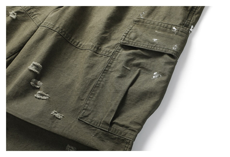 Close-up of olive cargo pants with a flap pocket, distressed white marks, and small frayed patches.