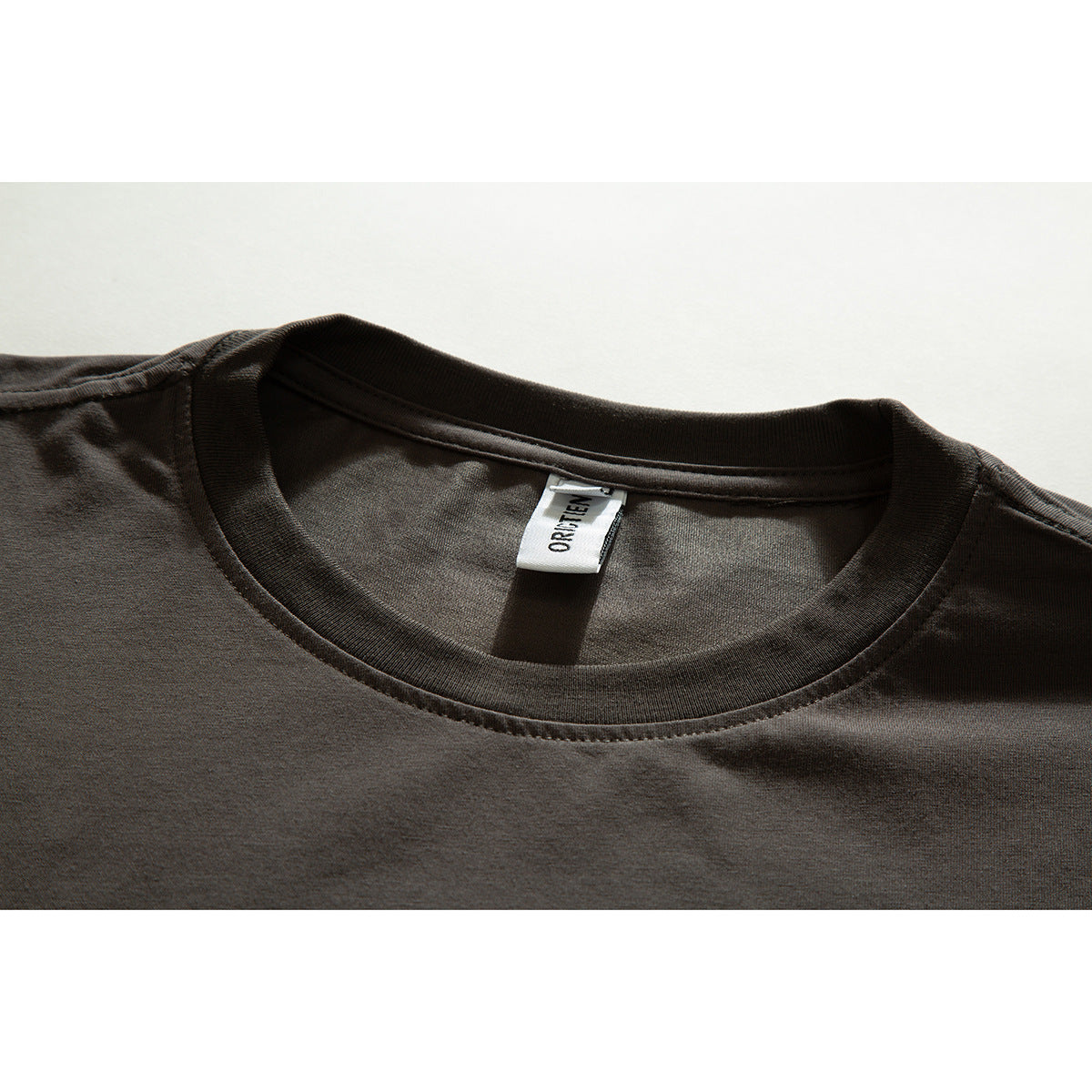 Close-up of a dark brown T-shirt's ribbed crew neck and sewn white inner label.