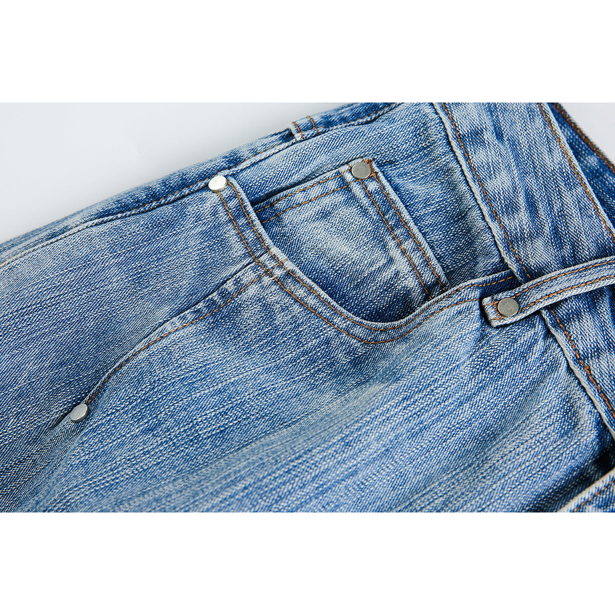 Close-up of a small front pocket and rivets on light blue faded jeans.