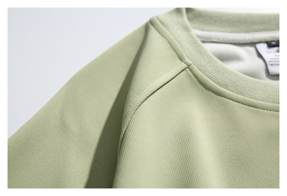 Close-up of a pale sage-green sweatshirt collar, shoulder seam, and partially visible neck tag.