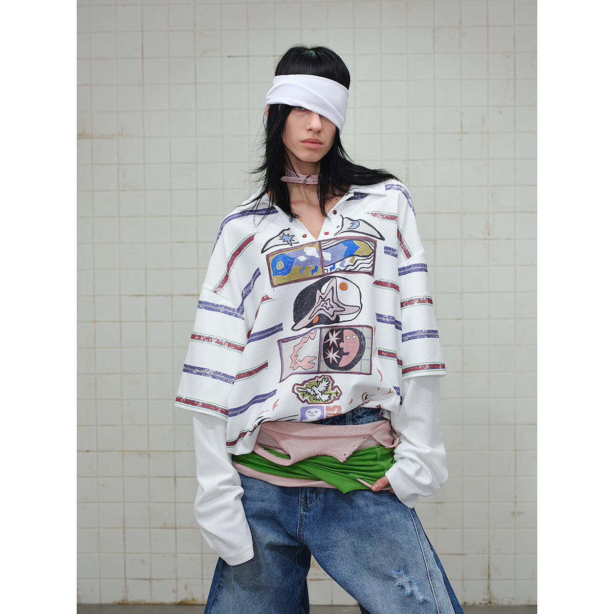 Model wearing an oversized white graphic polo with multicolor stripes and extra-long sleeves, paired with layered tops and