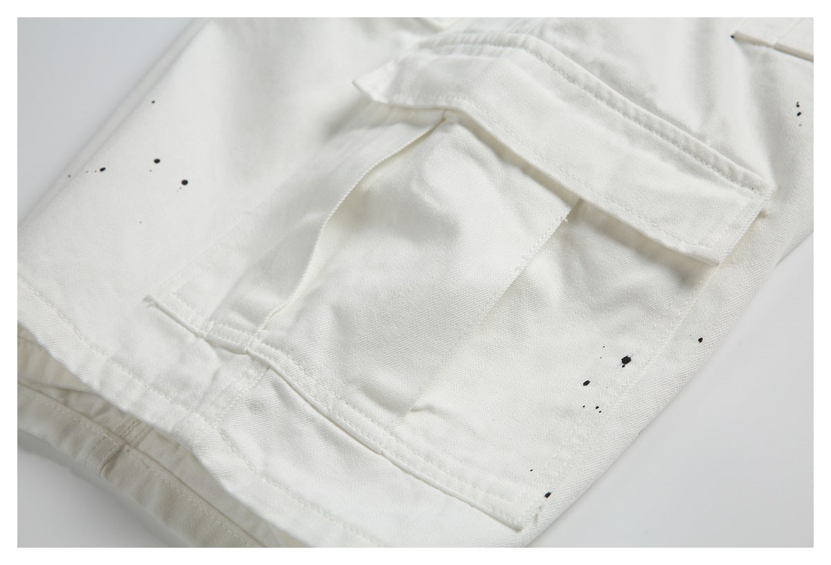 Close-up of a white garment with a layered stitched pocket flap and scattered small black specks.