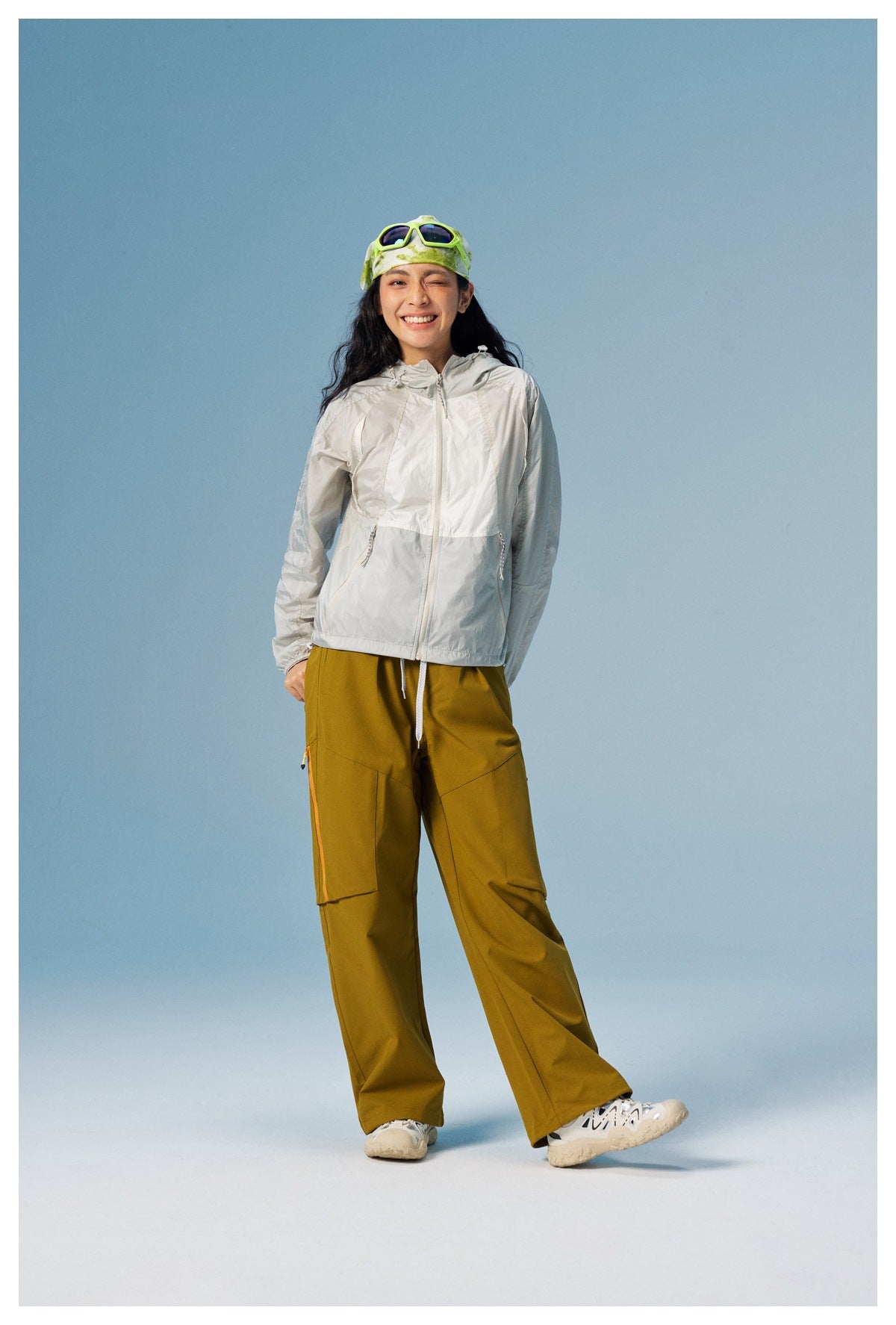 Model wearing the white hooded zip jacket with olive cargo pants, green bandana and sneakers against a blue backdrop