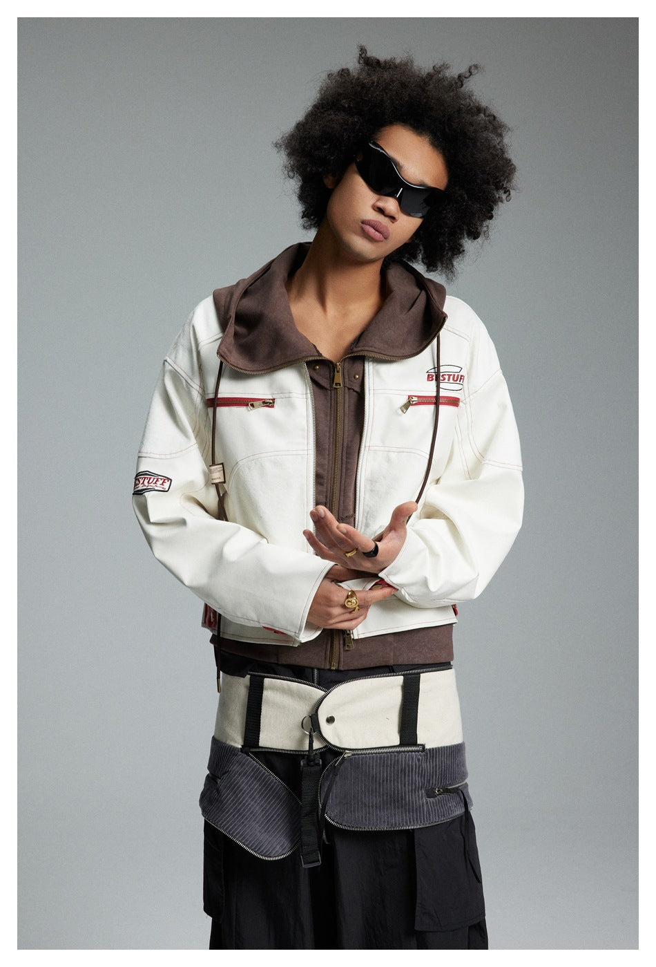 Model in a cream jacket with red zip pockets and brown hood, shown from the front with a layered brown zip top.
