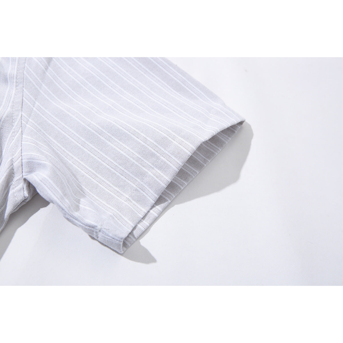 Close-up of the short sleeve and hem on a pale gray shirt with thin white stripes.