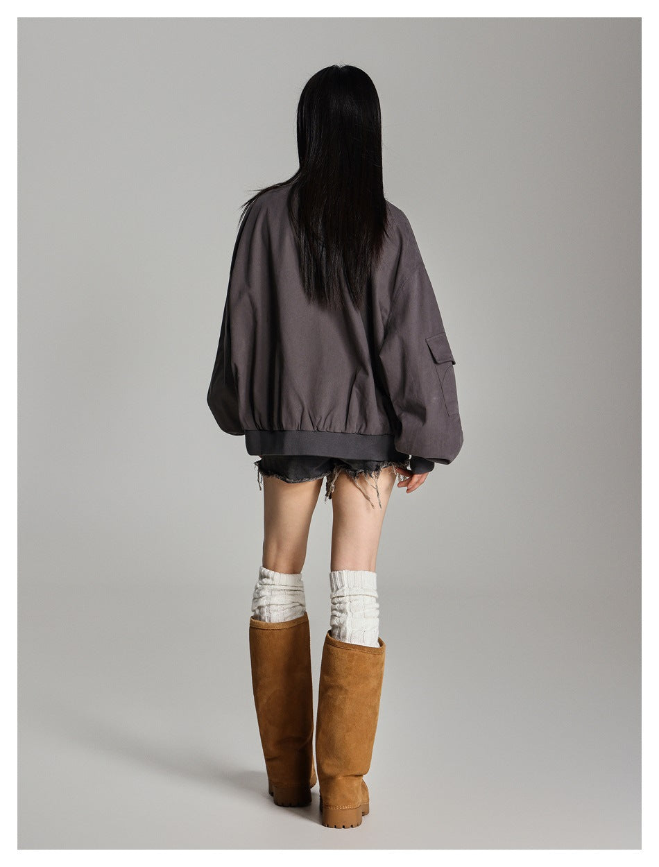 Rear view of a model wearing an oversized charcoal-gray jacket with a gathered hem and flap pocket on the sleeve.