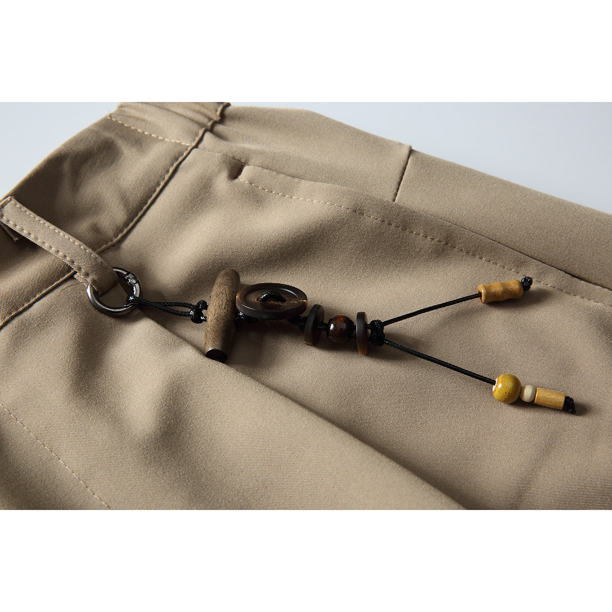 Close-up of beige trousers with a decorative cord and wooden beads attached near the waistband.