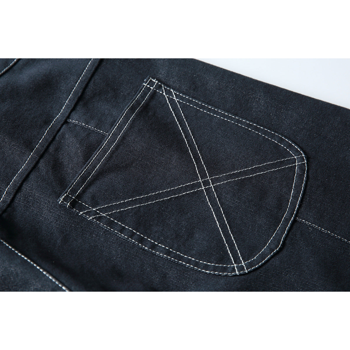 Close-up of a dark indigo trouser back pocket with prominent white geometric contrast stitching.