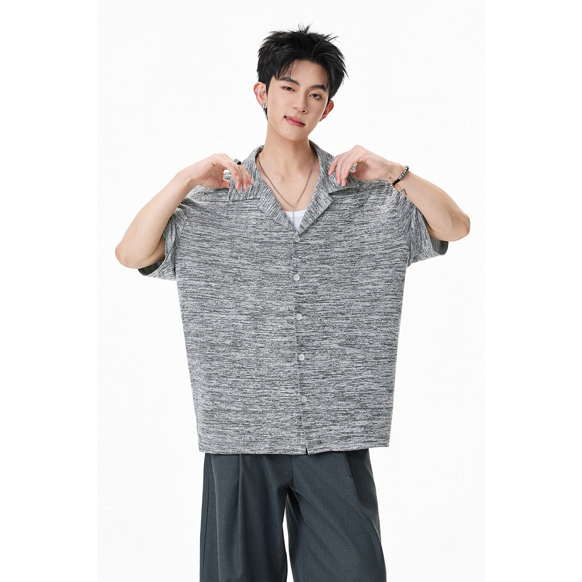Model holds out a gray marled short-sleeve button-front shirt, showing its loose fit and notched collar.