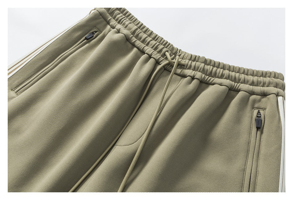 Close-up of olive jogger pants showing the elastic drawstring waist, zip pockets and white side stripe.