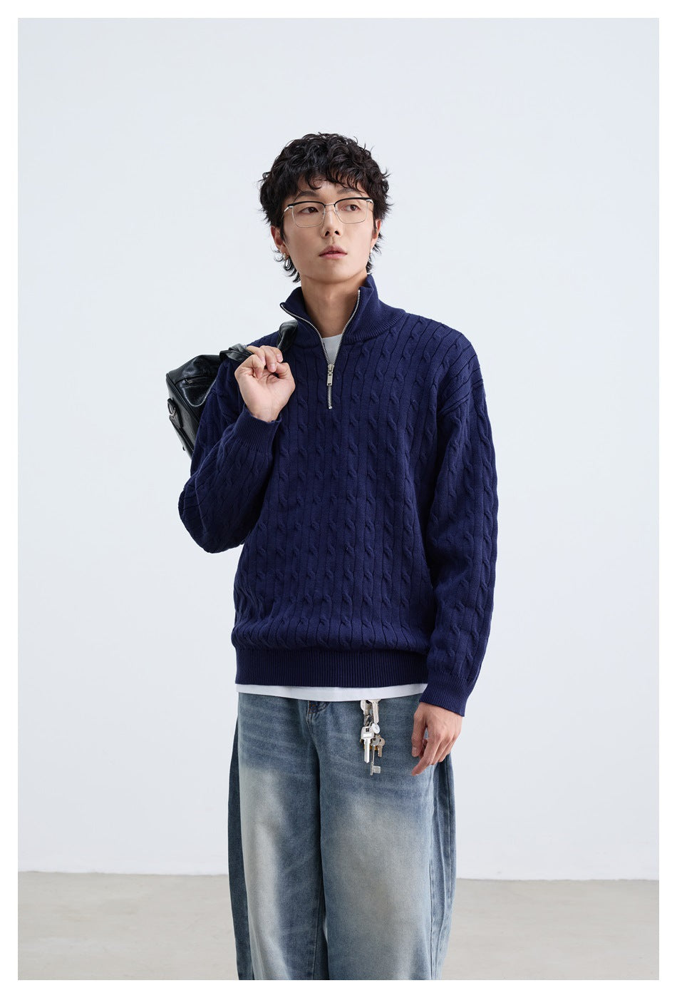 Front view of a model in a navy cable-knit quarter-zip sweater, shown with light-wash jeans.