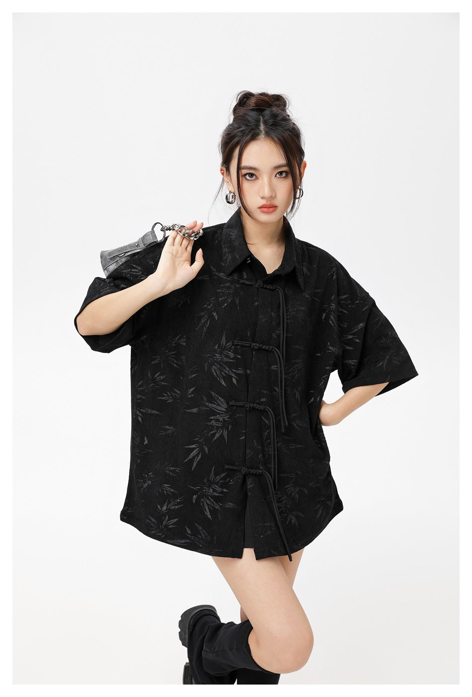 Closer view of a model wearing a black leaf-pattern shirt with a pointed collar and knotted front closures.