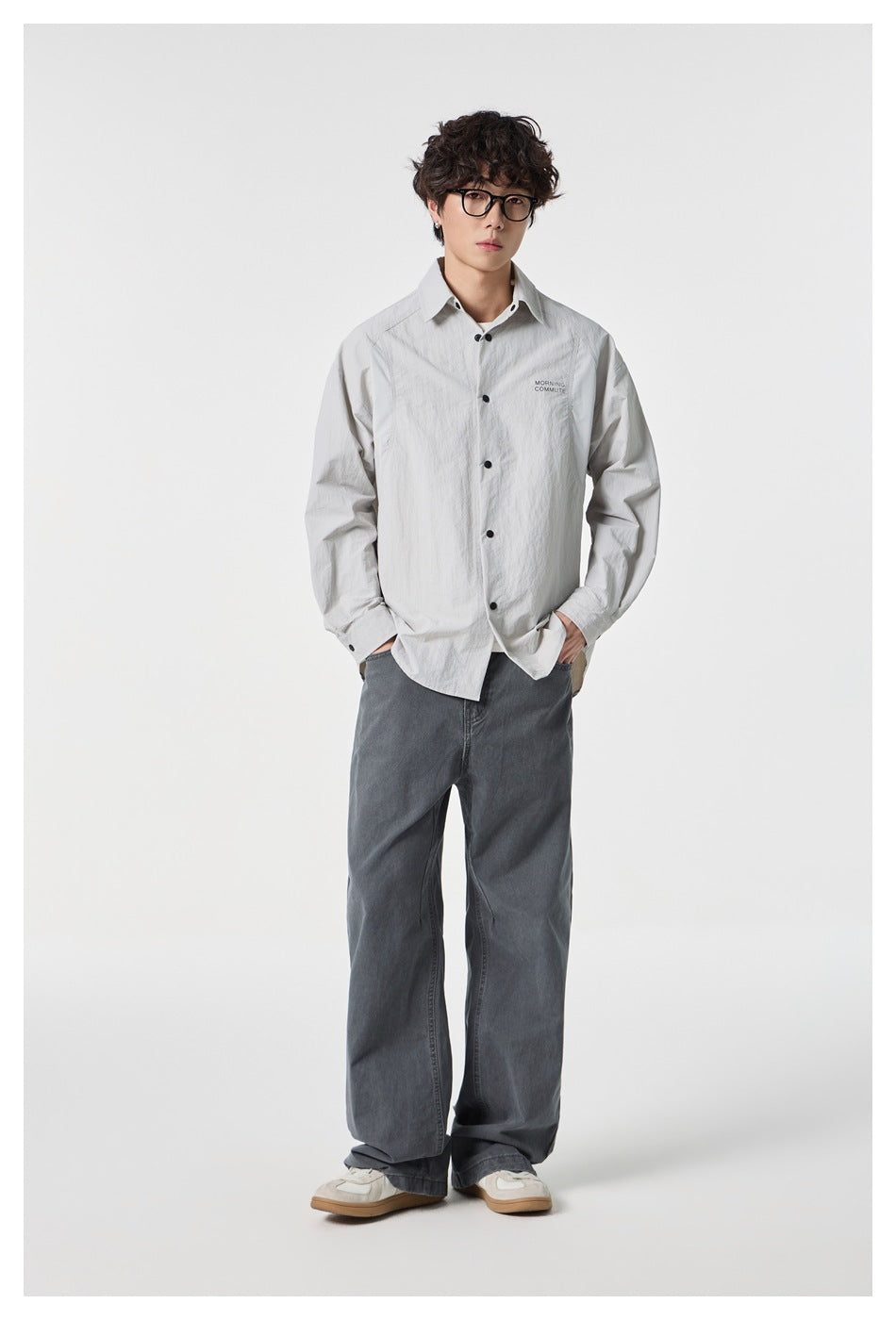 Model wearing a light gray button-up shirt with dark buttons and small chest lettering, paired with wide gray jeans.