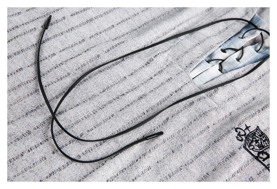 Close-up of black neckline lacing across a gray top with openwork stripes; part of an embroidered crest is visible.