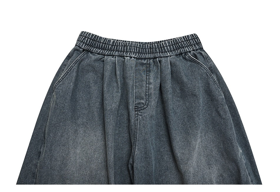 Close-up of the front waist of dark gray denim pants with an elastic waistband and pleated front.