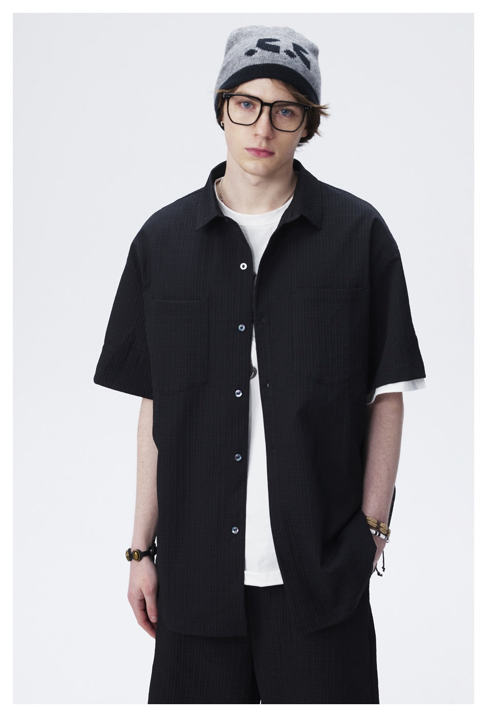 Model wearing a black short-sleeve button-up shirt with two chest pockets over a white T-shirt.