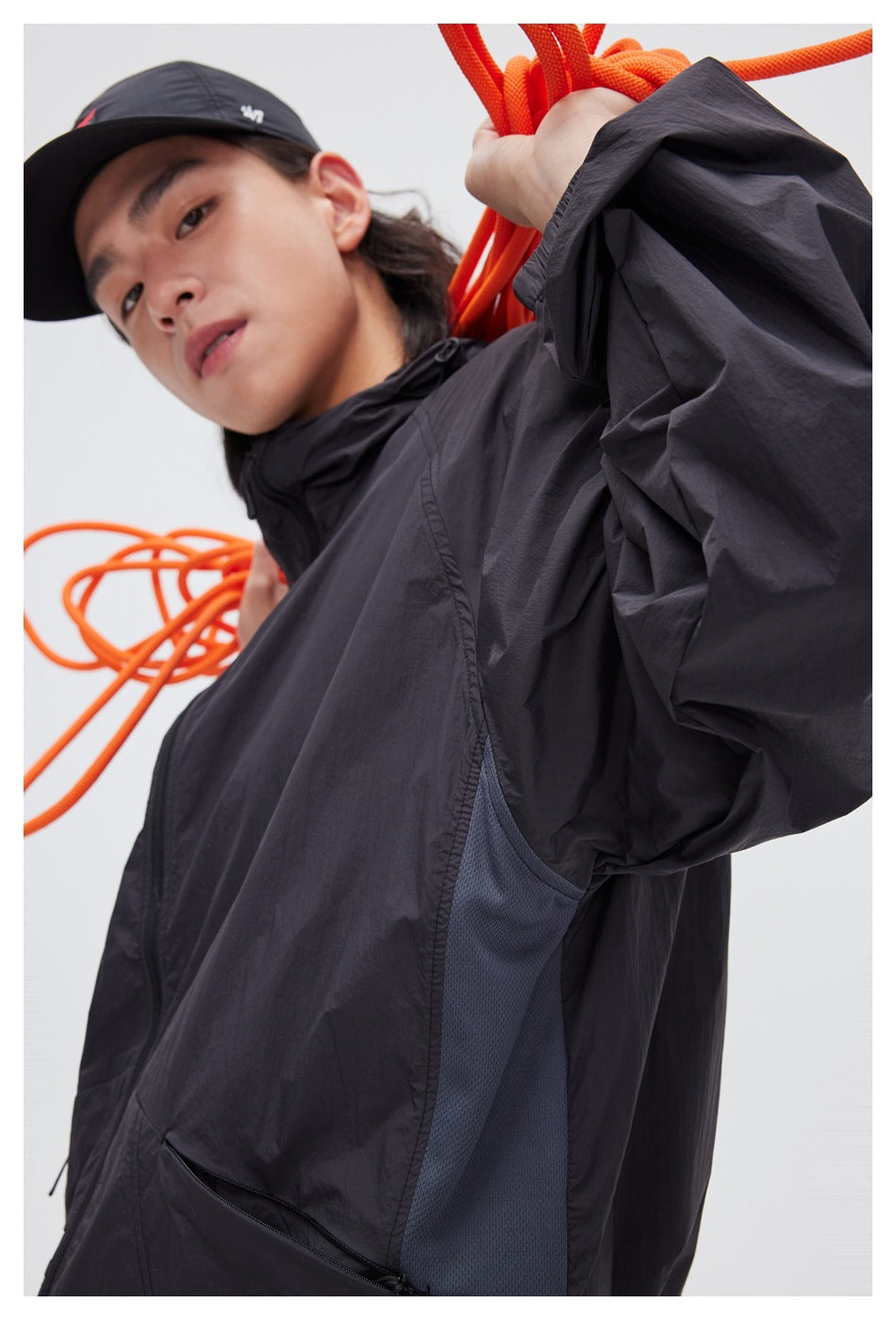 Close-up of a model wearing a black hooded jacket, showing the sleeve, side mesh panel, and zip pocket.