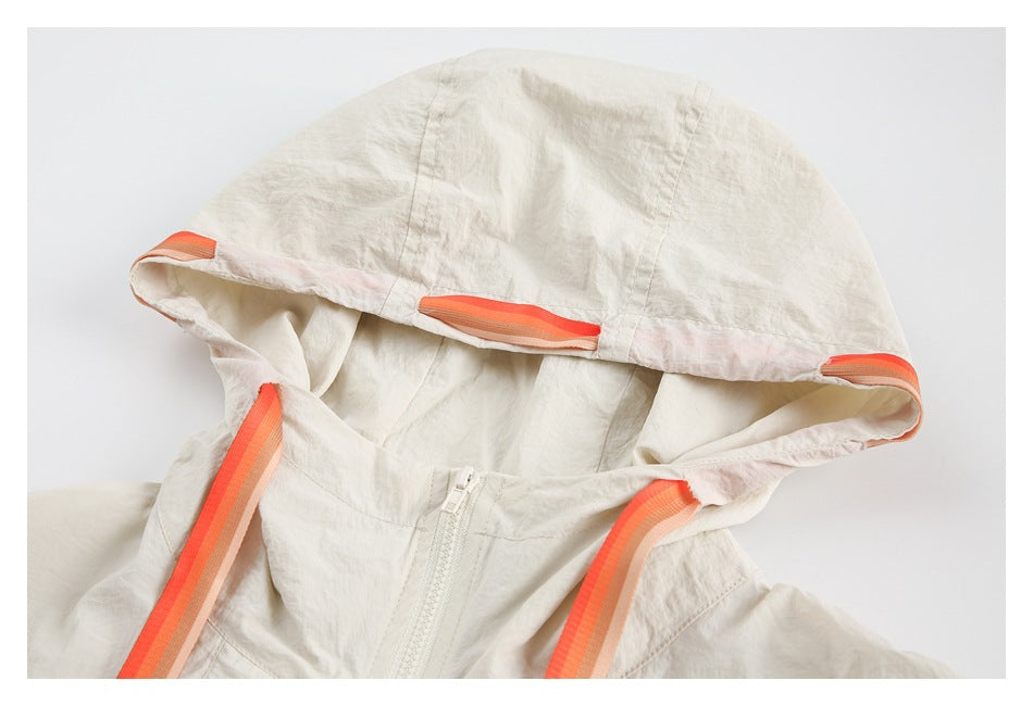 Close-up of a cream jacket hood with orange-striped trim and matching drawstrings.
