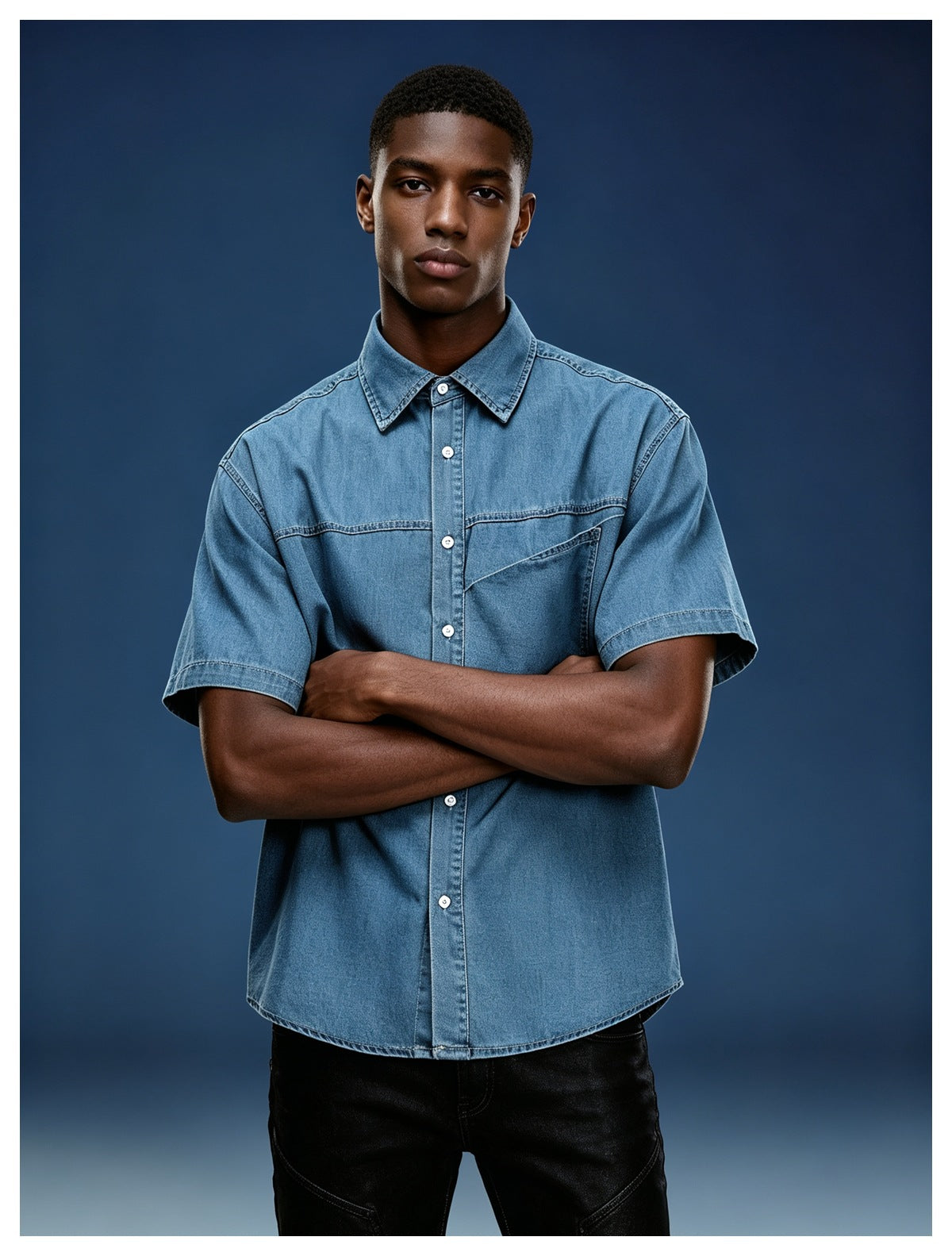 Man in washed blue short-sleeve denim-look shirt with chest pocket, arms crossed, against a dark blue background
