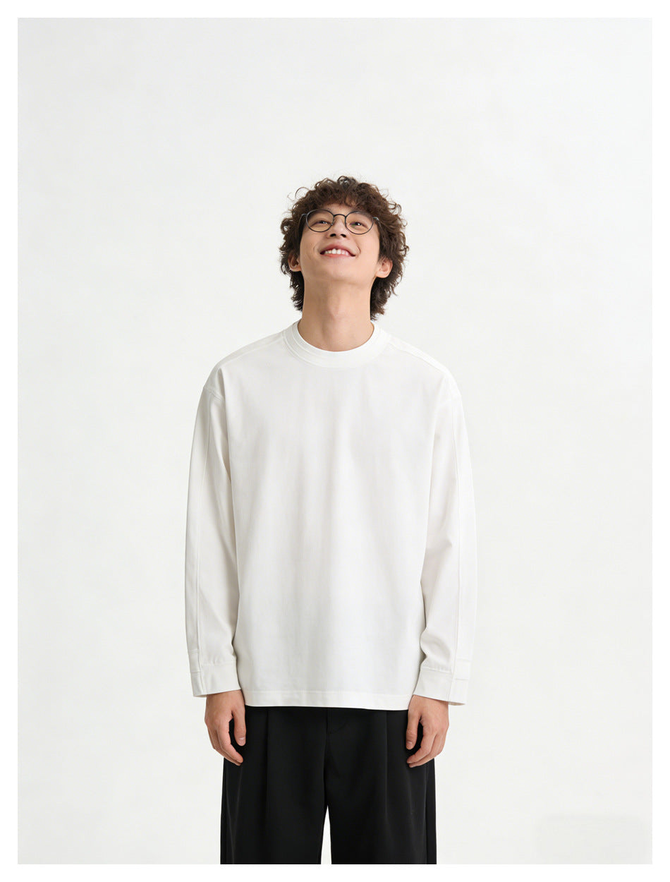 Model wearing a plain white long-sleeve crewneck shirt with black trousers, shown from the front.