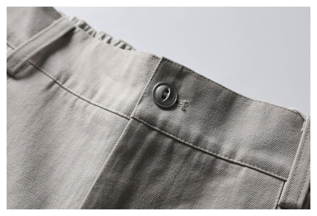 Close-up of gray herringbone trousers showing the waistband, belt loop, and dark button.