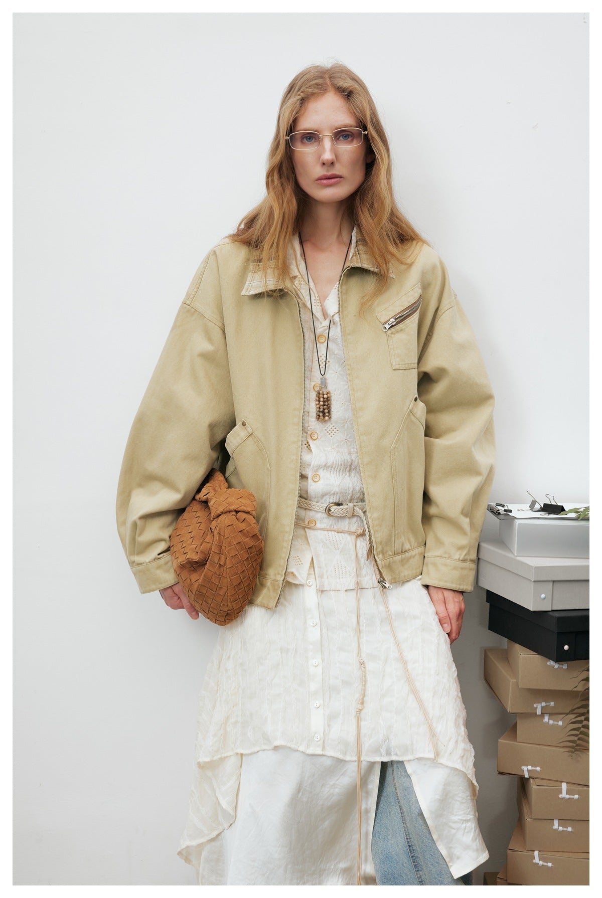 Front view of a model wearing a beige zip-front jacket over a long white layered dress.